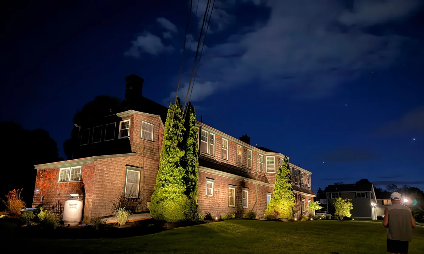 Cedar shingle colonial home lit at night with professional landscape uplighting